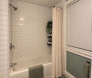 Un baño con ducha, bañera y ventana con persianas.