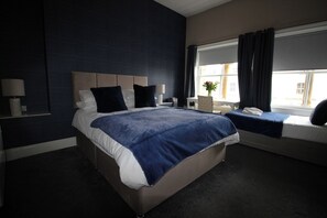A hotel room with a large bed, bedside tables, a window with curtains, and a view of the outside. - Cornerhouse Apartment 2 (Llandudno)