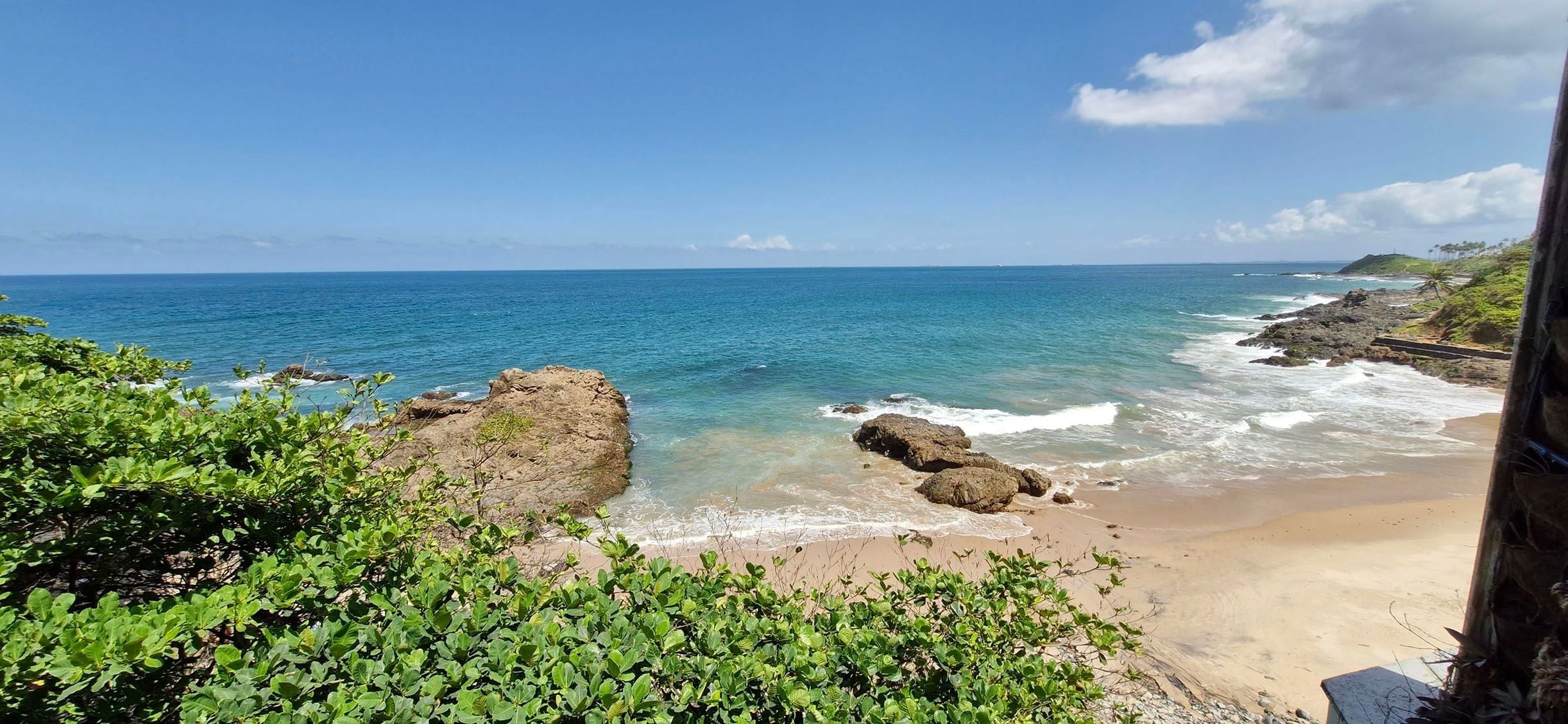 A coastal landscape with a sandy beach, rocky outcrops, and clear blue sea.