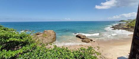 A coastal landscape with a sandy beach, rocky outcrops, and clear blue sea.