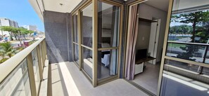 A balcony with a glass door leading to a room with a bed and a TV. - COOND0126 - Beach Class Salvador (Salvador)