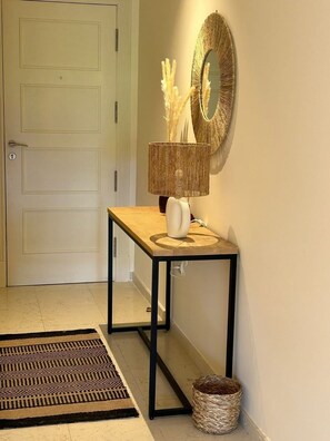 Un couloir avec une porte blanche, une console en bois surmontée d’une lampe, un miroir et un panier en osier.