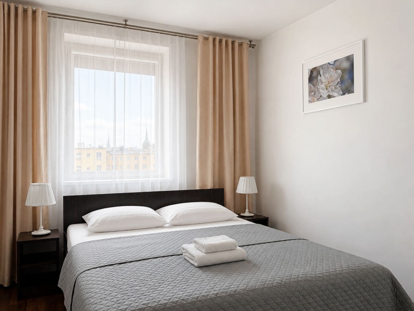 Quarto de hotel com uma cama grande, duas mesinhas de cabeceira, uma janela com cortinas e um quadro na parede.