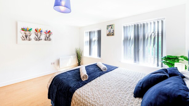 Ein Schlafzimmer mit einem Bett, einer blauen Lampe, einem Fenster mit Jalousien und Wandbildern.