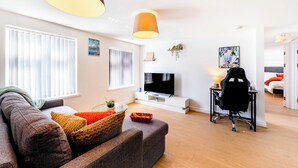 Ein modernes Wohnzimmer mit einer Couch, einem Fernseher und einem Schreibtisch mit Stuhl.