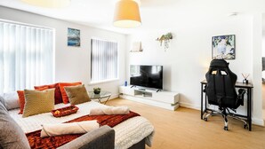 Ein modernes Wohnzimmer mit einer Couch, einem Fernseher und einem Schreibtisch mit Stuhl.