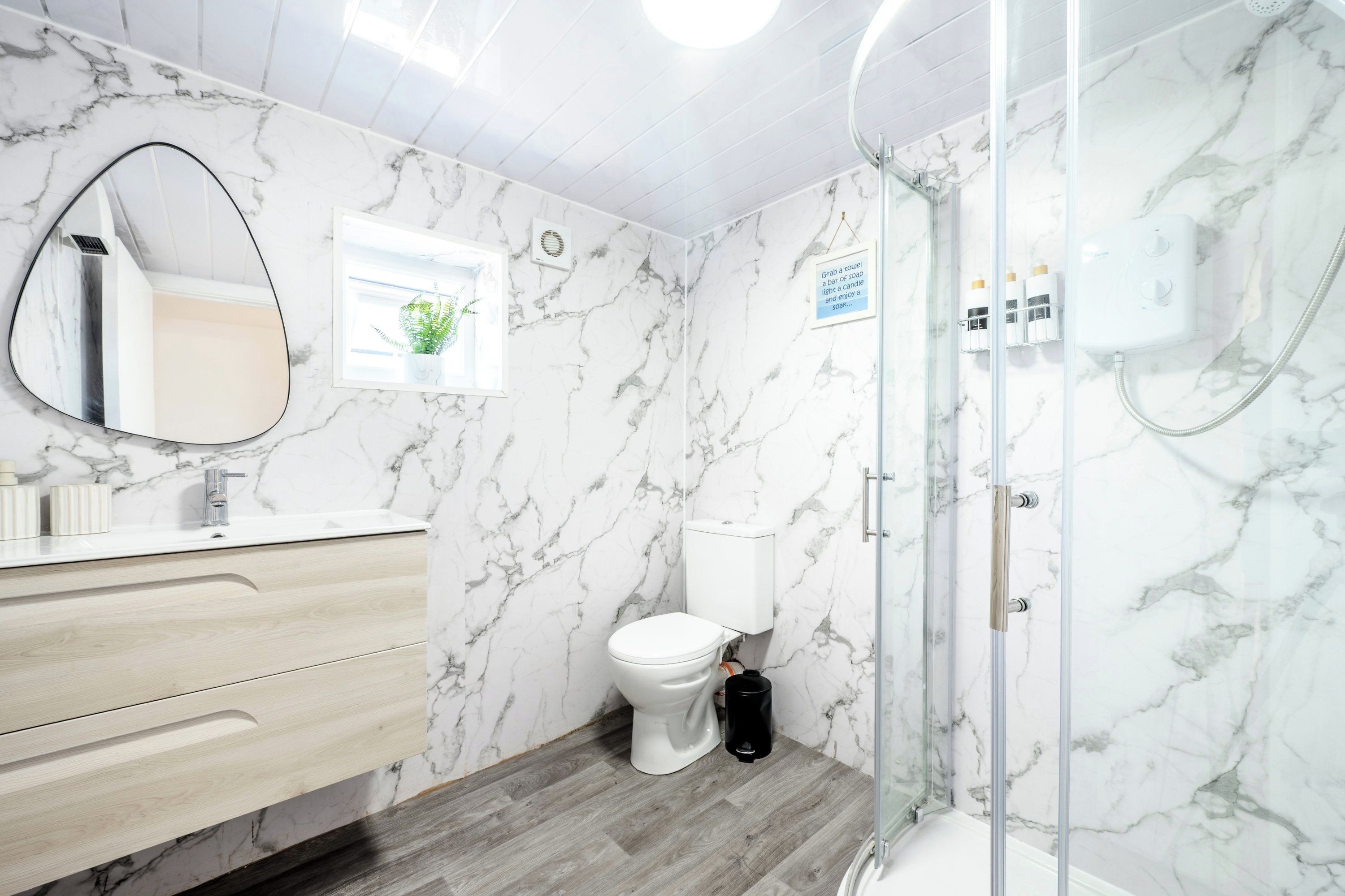 A bathroom with a marble wall, a wooden vanity, a toilet, and a glass-enclosed shower.