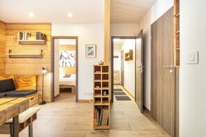 A modern interior with a wooden floor, a bed with a white headboard, a bookshelf, and a desk with a lamp. - travelski home premium - Résidence La Mariande - 2 Pièces cabine 4 personnes N°1.6 (Les Deux Alpes)