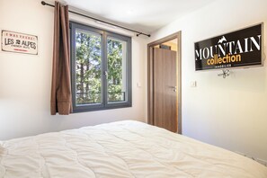 Ein Schlafzimmer mit einem Bett, einem Fenster mit Vorhängen, einer Tür und einem Wandzeichen.