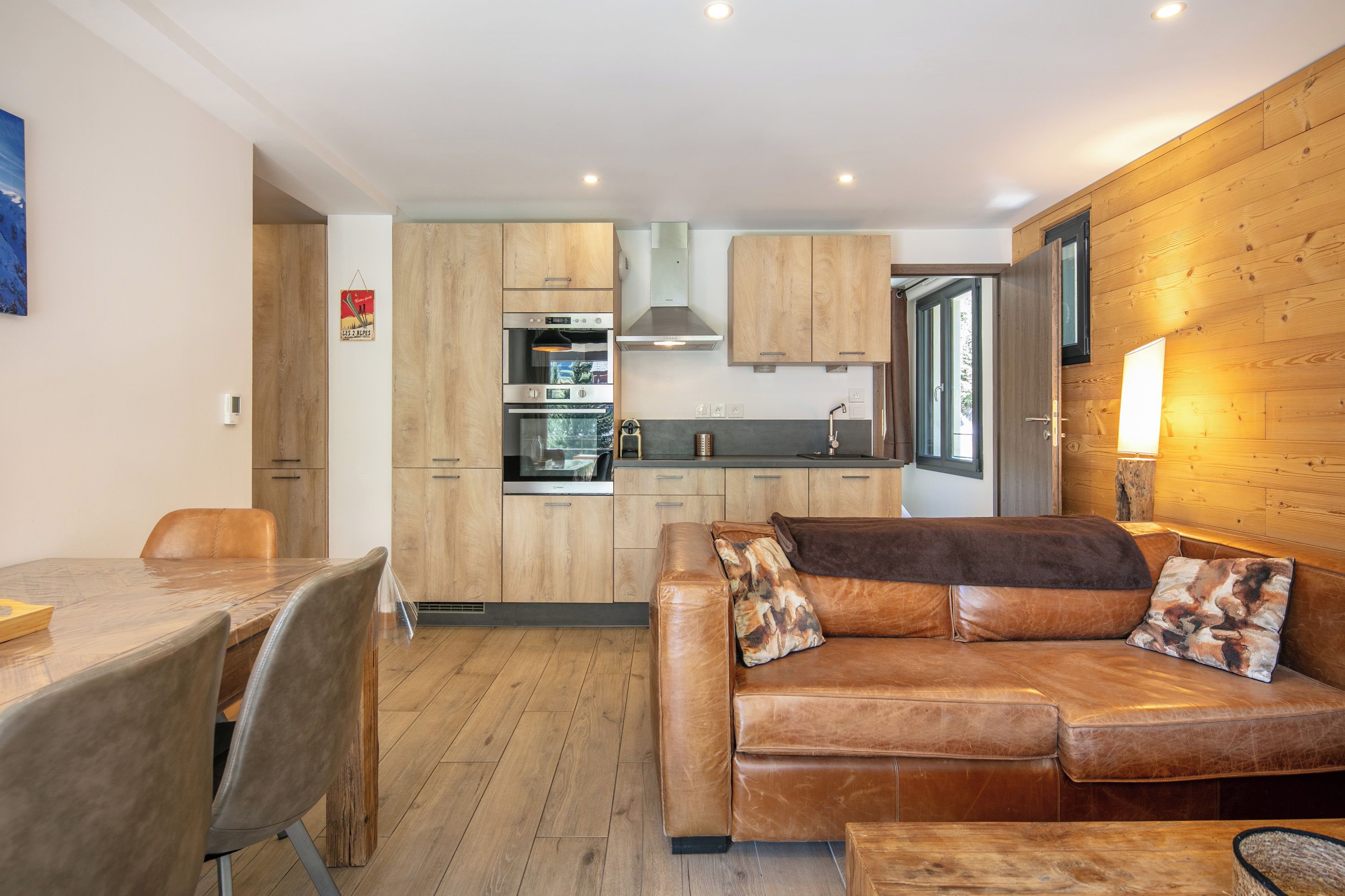 Una cucina moderna con mobili in legno, un'area pranzo con tavolo e sedie, e un divano in pelle con cuscini.