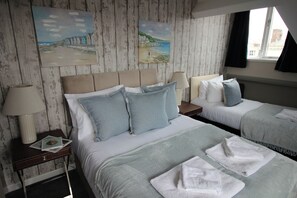 A hotel room with two beds, a wooden headboard, bedside lamps, and artwork on the wall. - Cornerhouse Apartment 4 (Llandudno)