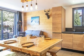 A modern kitchen with wooden cabinets, a dining table set for four, and a large window offering a view of the outdoors. - travelski home premium - Résidence La Mariande - 3 Pièces 6 personnes N°3.1 (Les Deux Alpes)