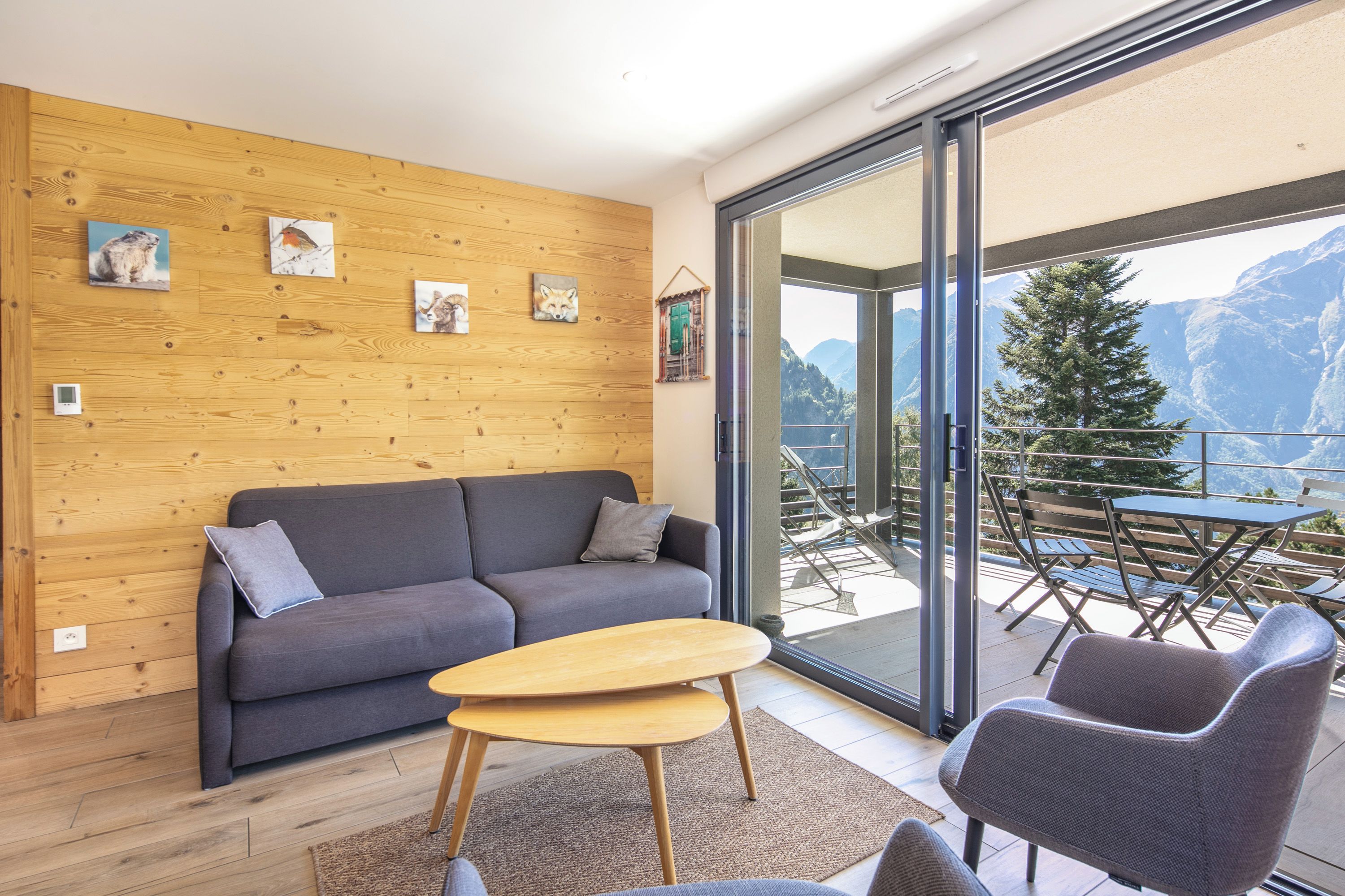 Ein modernes Wohnzimmer mit grauem Sofa, Holzwand und Balkon mit Tisch und Stühlen.