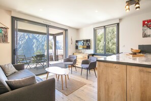 A modern interior with a kitchen, dining area, and a view of mountains through large windows. - travelski home premium - Résidence La Mariande - 3 Pièces 6 personnes N°3.3 (Les Deux Alpes)