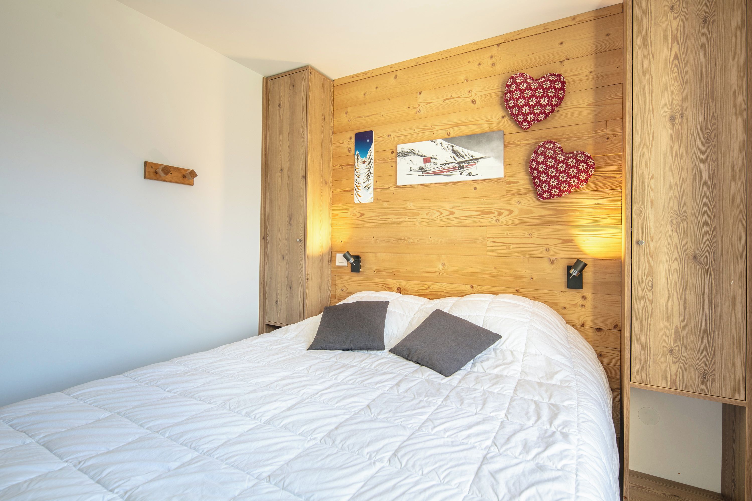 A bedroom with a wooden headboard, a bed with white bedding, two pillows, and wall-mounted artwork.