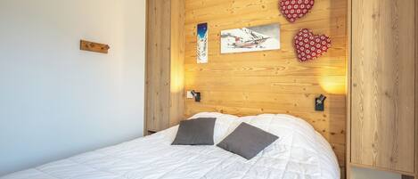 Ein Schlafzimmer mit einem Holzkopfteil, einem Bett mit weißer Bettwäsche, zwei Kissen und einem an der Wand hängenden Kunstwerk.
