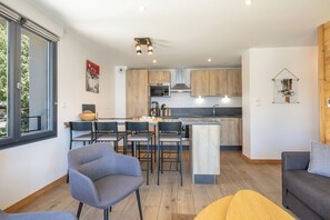 A modern kitchen with wooden cabinets, a central island, and a dining area with chairs. - travelski home premium - Résidence La Mariande - 3 Pièces 6 personnes N°3.3 (Les Deux Alpes)