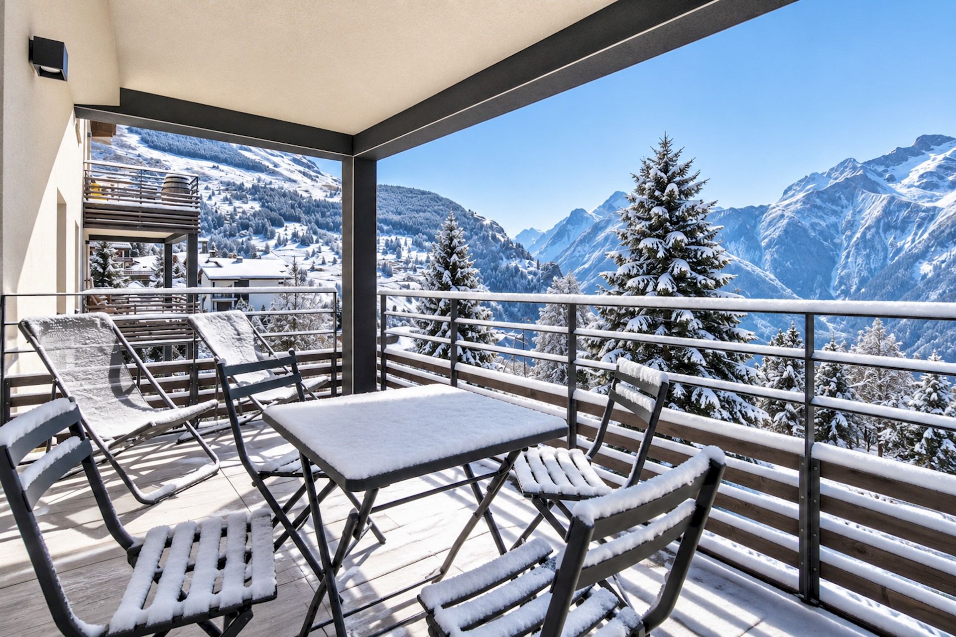 Een balkon met een tafel en stoelen, met uitzicht op een besneeuwd berglandschap.