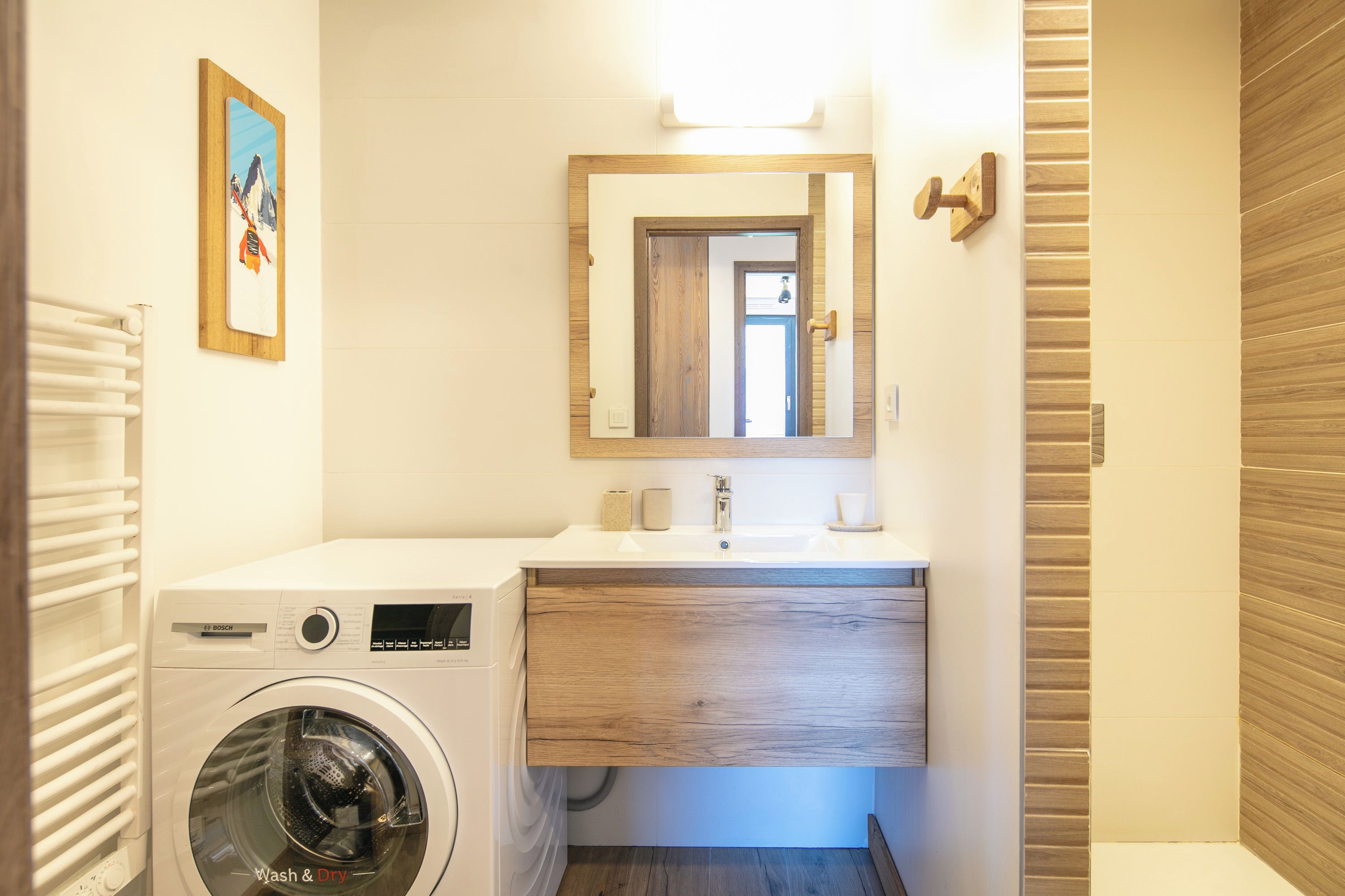 Une petite salle de bain équipée d’un lave-linge, d’un lavabo avec un meuble-vasque en bois et d’un miroir.