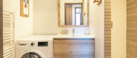 Une petite salle de bain équipée d’un lave-linge, d’un lavabo avec un meuble-vasque en bois et d’un miroir.