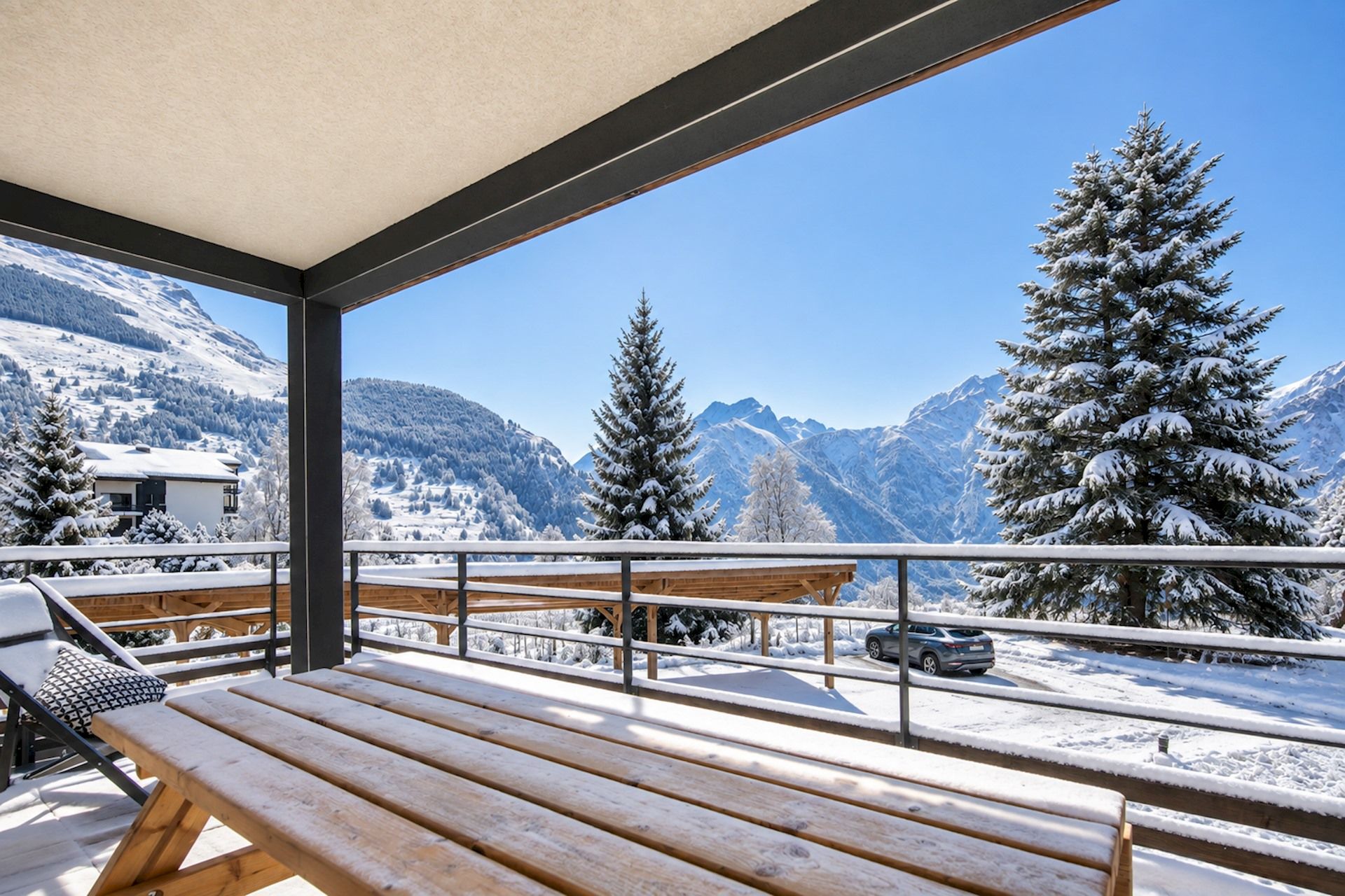 A wooden deck with a bench, a car parked in the background, and a mountain view.