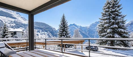 A wooden deck with a bench, a car parked in the background, and a mountain view.