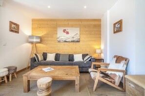 A cozy living room with a wooden wall, a sofa, a coffee table, and a chair. - travelski home premium - Résidence La Mariande - 4 Pièces 8 personnes N°1.2 (Les Deux Alpes)