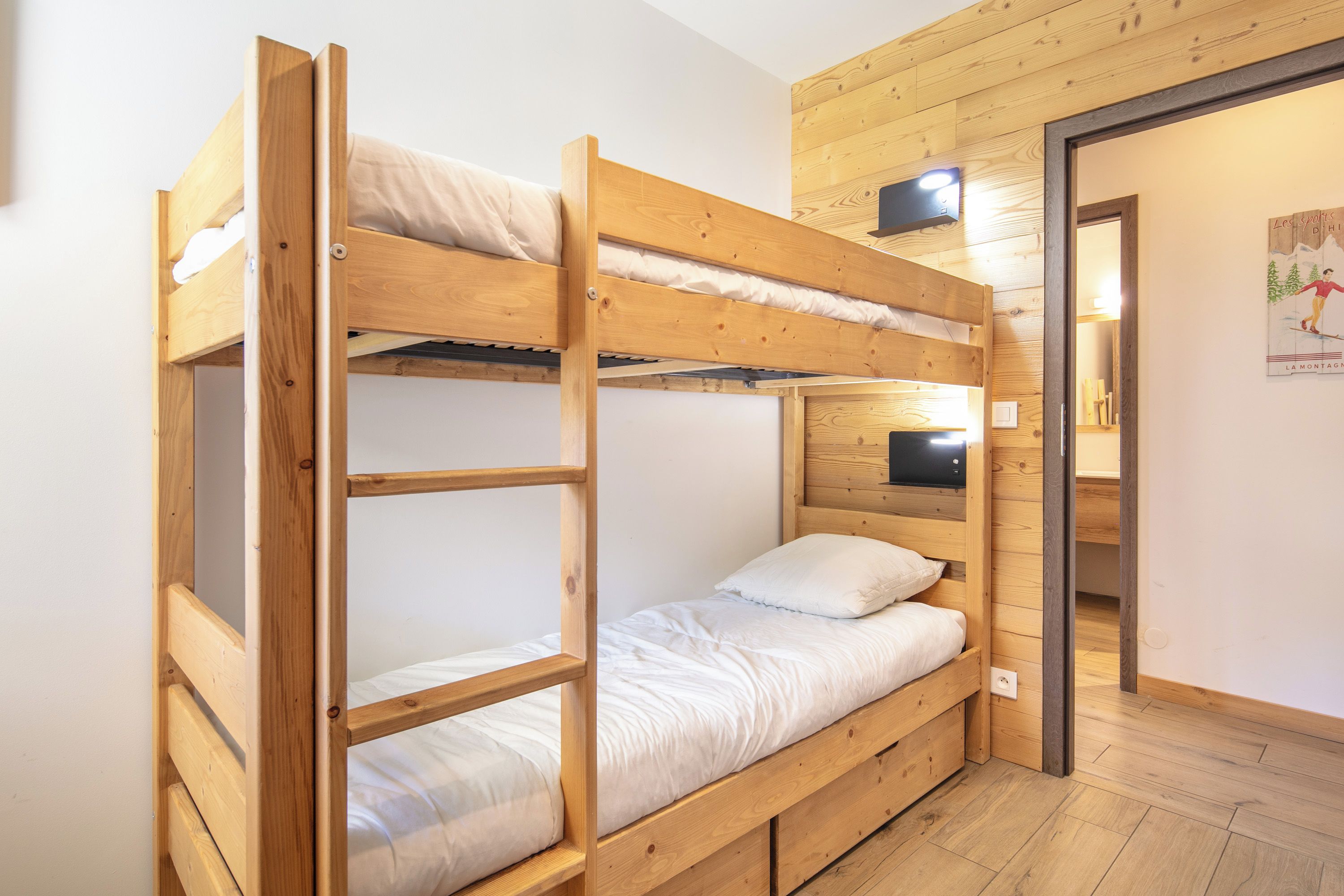 A bunk bed room with a wooden headboard, a wall-mounted light, and a door leading to another room.