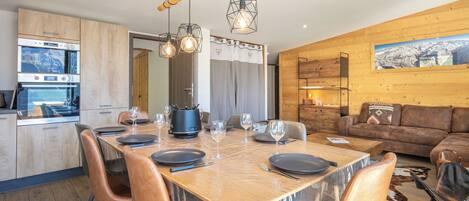 A modern kitchen with built-in appliances, a dining area with a wooden table and chairs, and a living room with a sofa and a mounted picture.