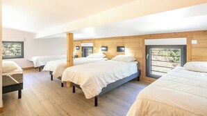 Quarto com quatro camas dispostas em fila, paredes de madeira e uma janela ampla que oferece luz natural.