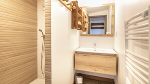 Casa de banho com chuveiro em estrutura de madeira, pia com espelho e porta-toalhas.