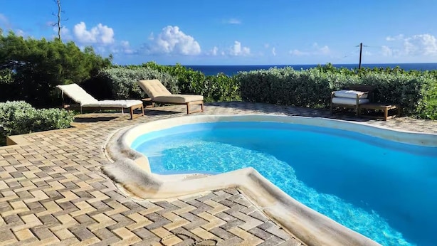 En swimmingpool med buet kant, omgivet af en flisebelagt terrasse og liggestole.