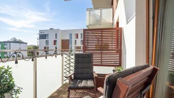A balcony with a wooden chair and a small table, a potted plant, and a view of a building with multiple windows.