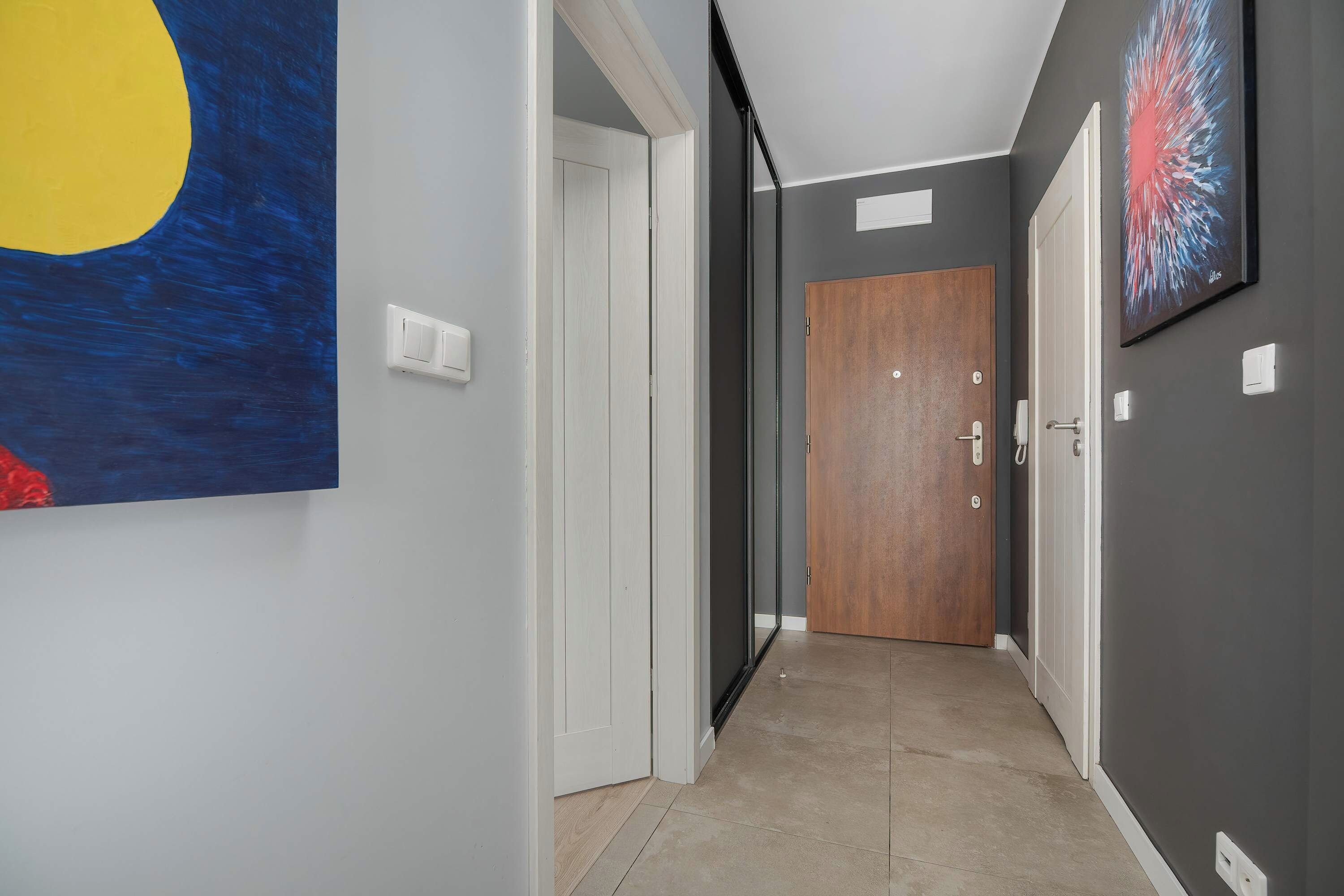 Un couloir avec une porte en bois, un interrupteur et un tableau accroché au mur.