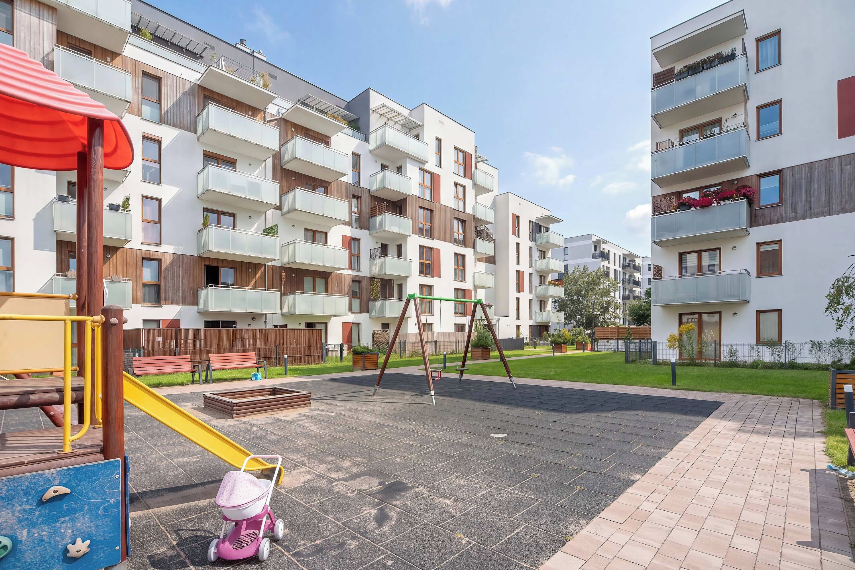 Um parquinho com escorrega e balanços, cercado por prédios de apartamentos com sacadas.