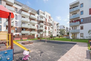 Un parque infantil con tobogán y columpios, rodeado de edificios de apartamentos con balcones.