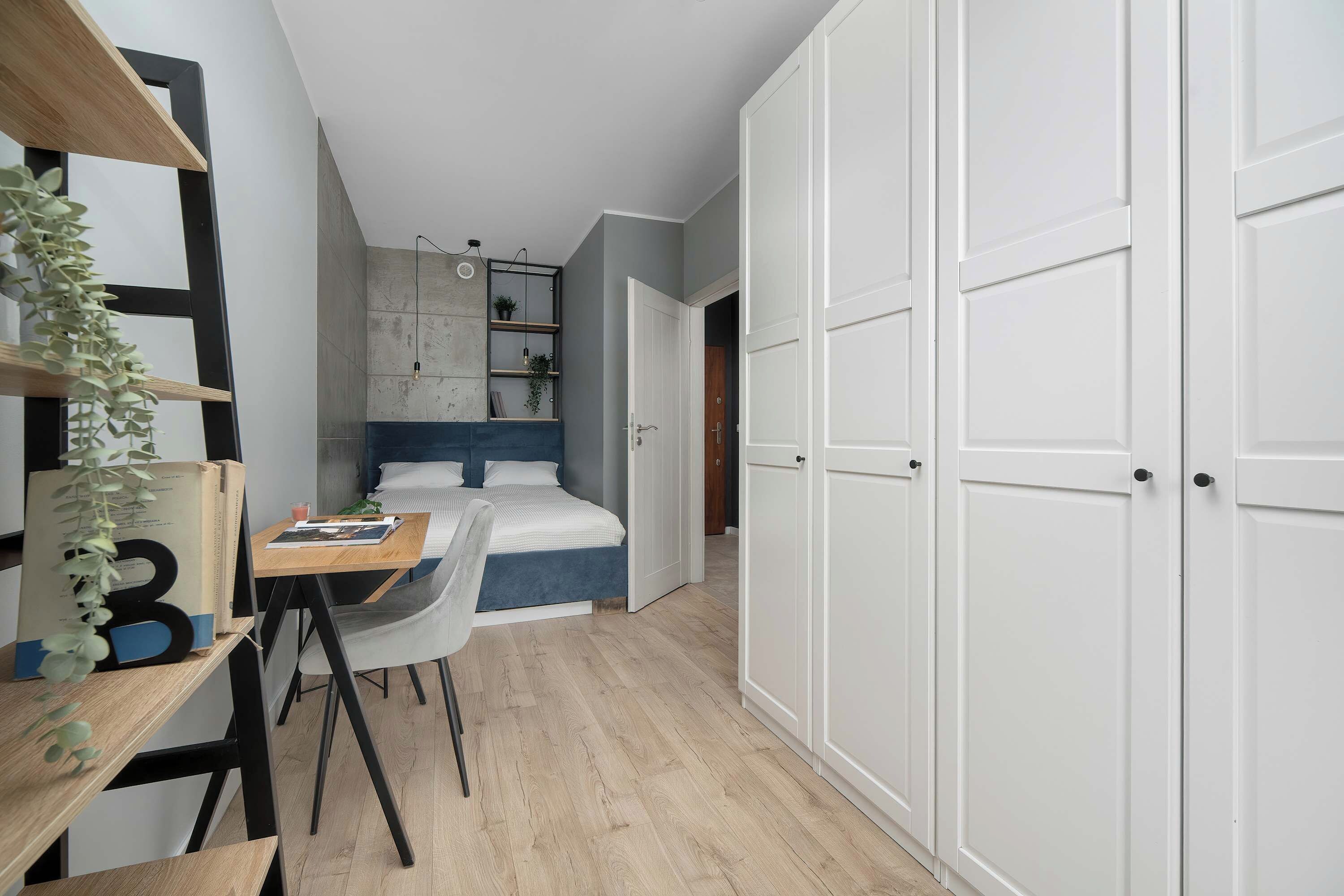 Quarto com cama, escrivaninha com cadeira, guarda-roupa e estante com plantas.