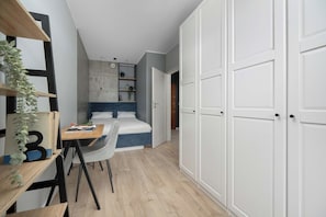 Un dormitorio con cama, escritorio y silla, armario y estantería con plantas.