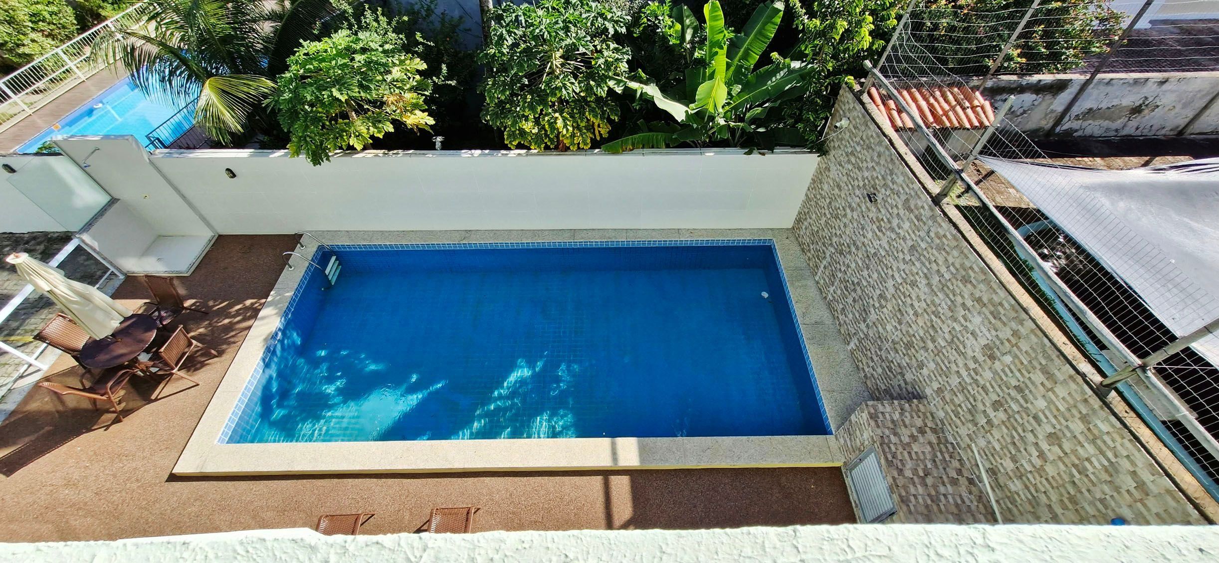 Une piscine rectangulaire dont les bords sont recouverts de carreaux, entourée d’un mur blanc et d’une clôture en métal.