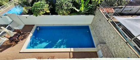 A rectangular swimming pool with a tiled edge, surrounded by a white wall and a metal fence.