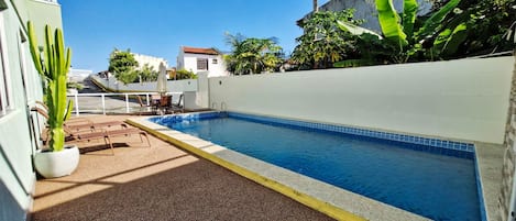 A swimming pool with a tiled edge, surrounded by a white wall and a gravel area.