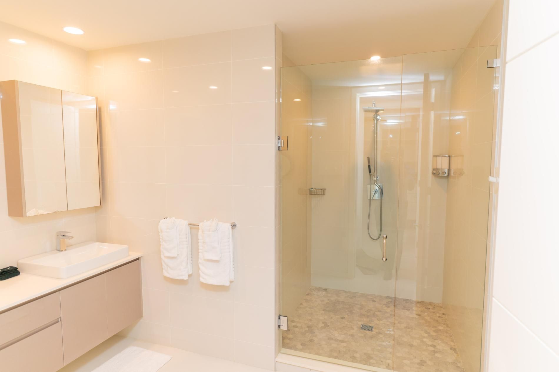 A modern bathroom with a glass-enclosed shower, a vanity with a sink, and two towels hanging on the wall.
