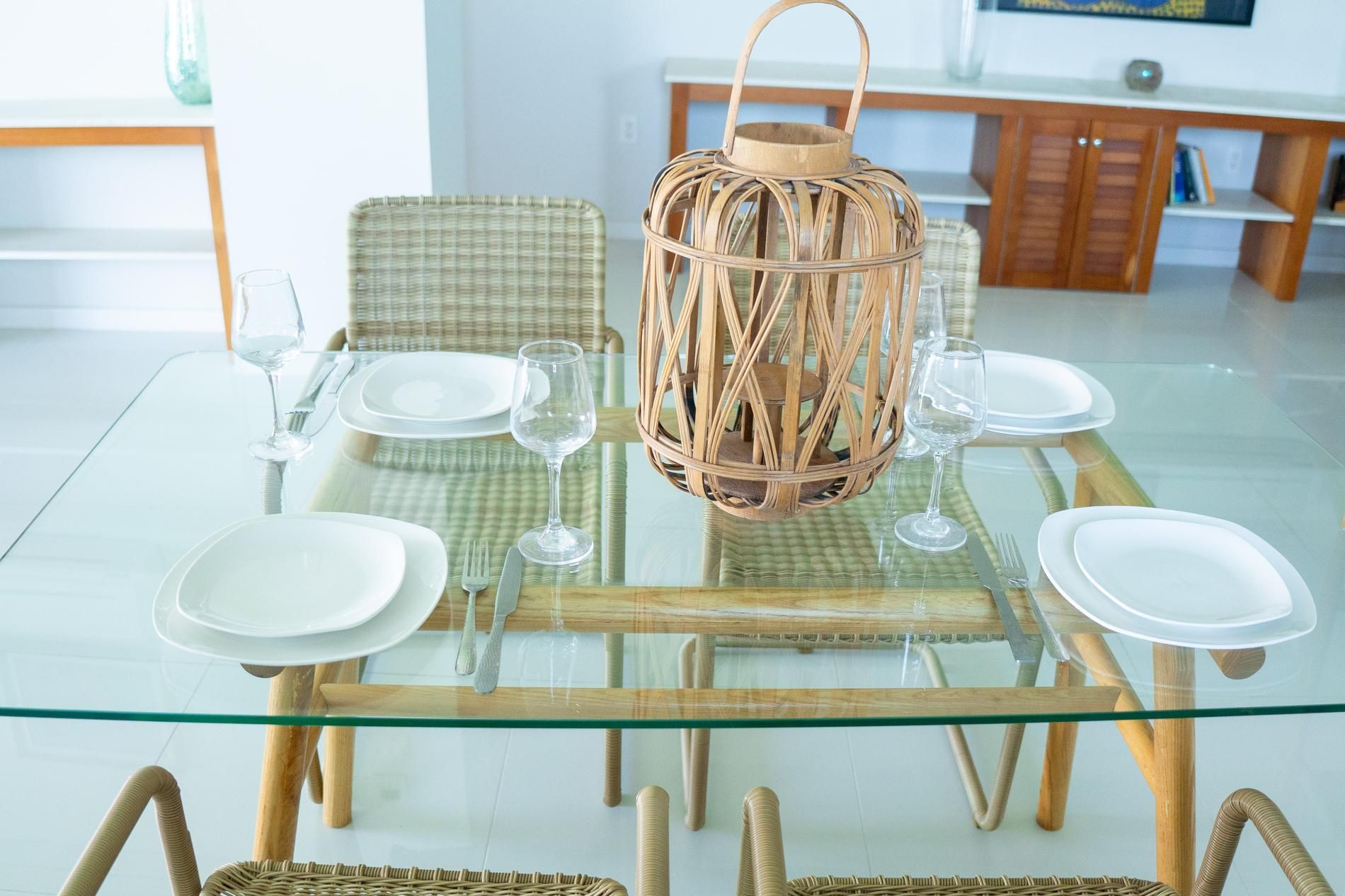 Une table à manger dressée avec de l’argenterie blanche, de la verrerie transparente et une lanterne tressée en guise de centre de table.
