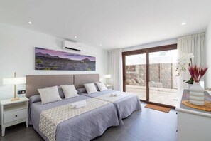 Ein Hotelzimmer mit einem großen Bett, zwei Nachttischen, einem Gemälde an der Wand und Blick durch eine Glastür.