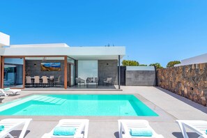 Ein modernes Haus mit Swimmingpool, Sitzgelegenheiten im Freien und einer Steinmauer.