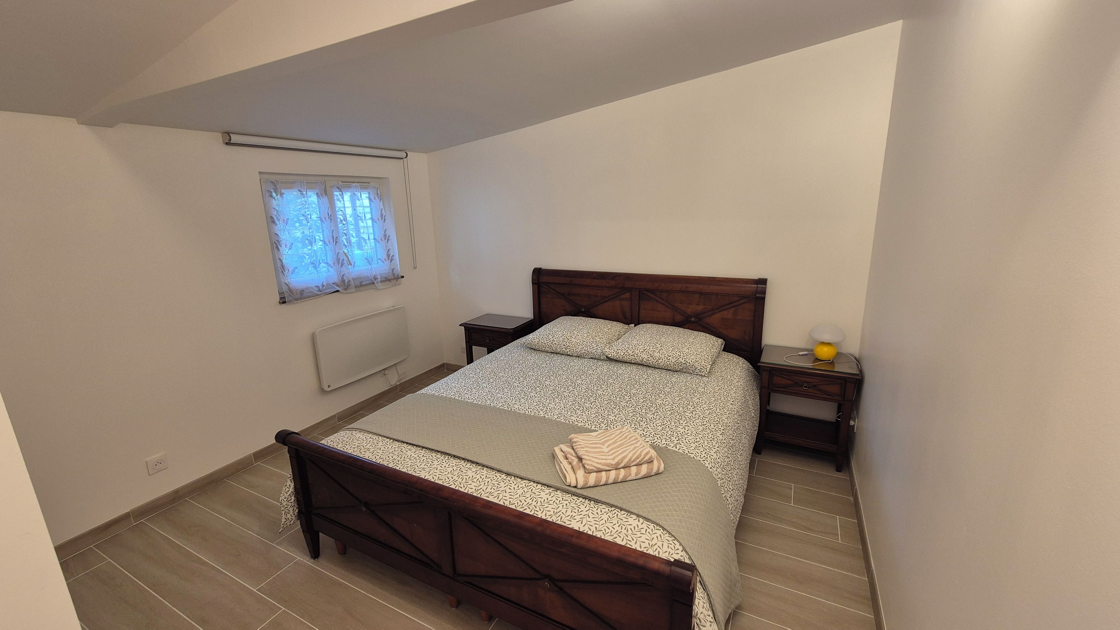 A bedroom with a bed, bedside tables, a window with curtains, and a radiator.