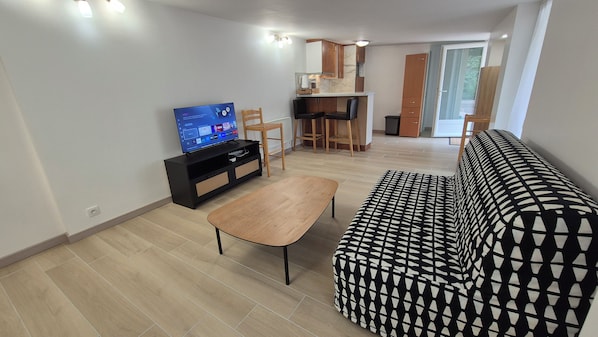 A living room with a sofa, a coffee table, a TV, and a dining area with chairs and a table.