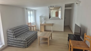 A compact living space with a sofa, a small desk, a chair, and a television.