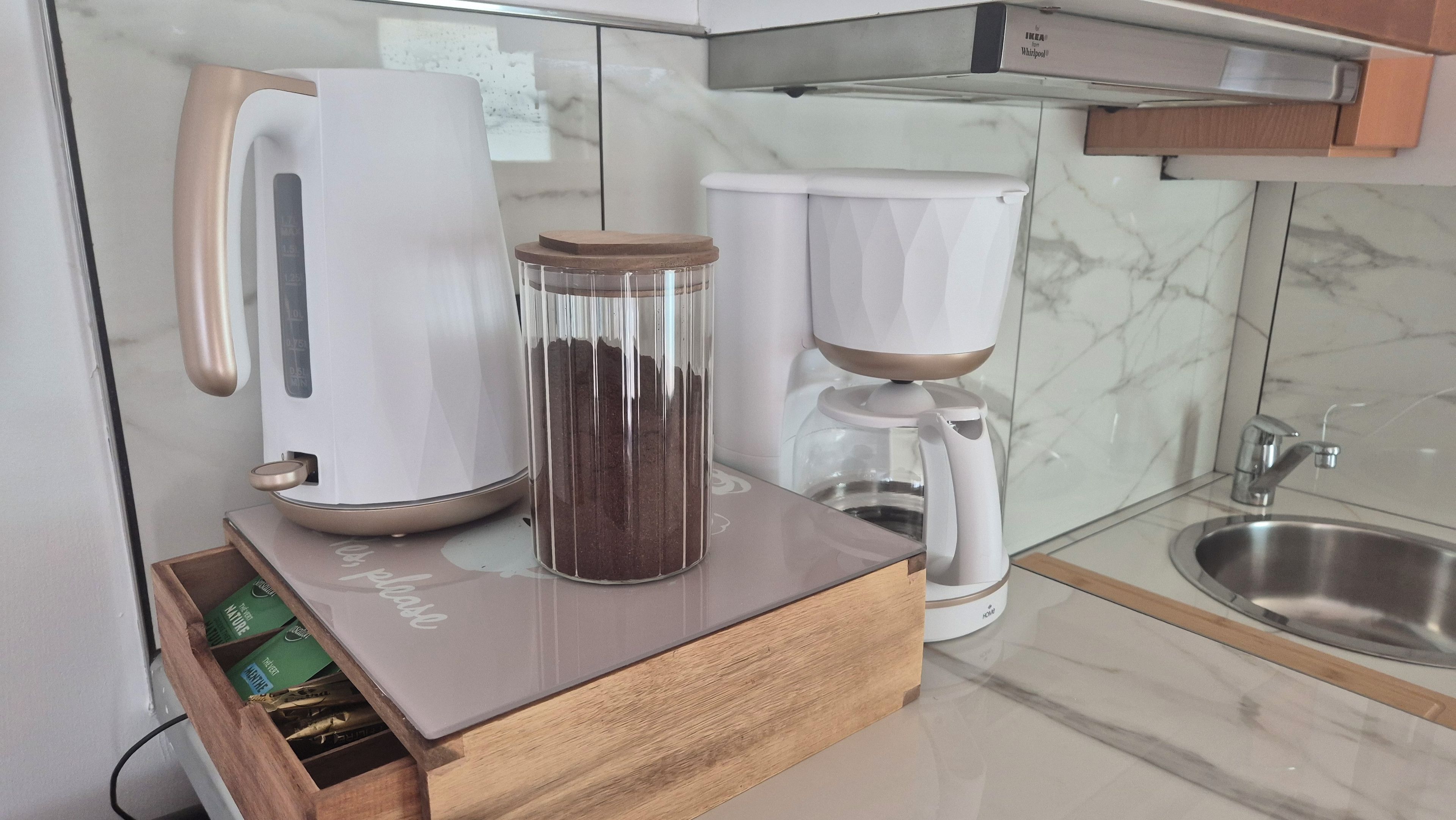 A kitchen with a coffee maker, a kettle, and a drawer unit.