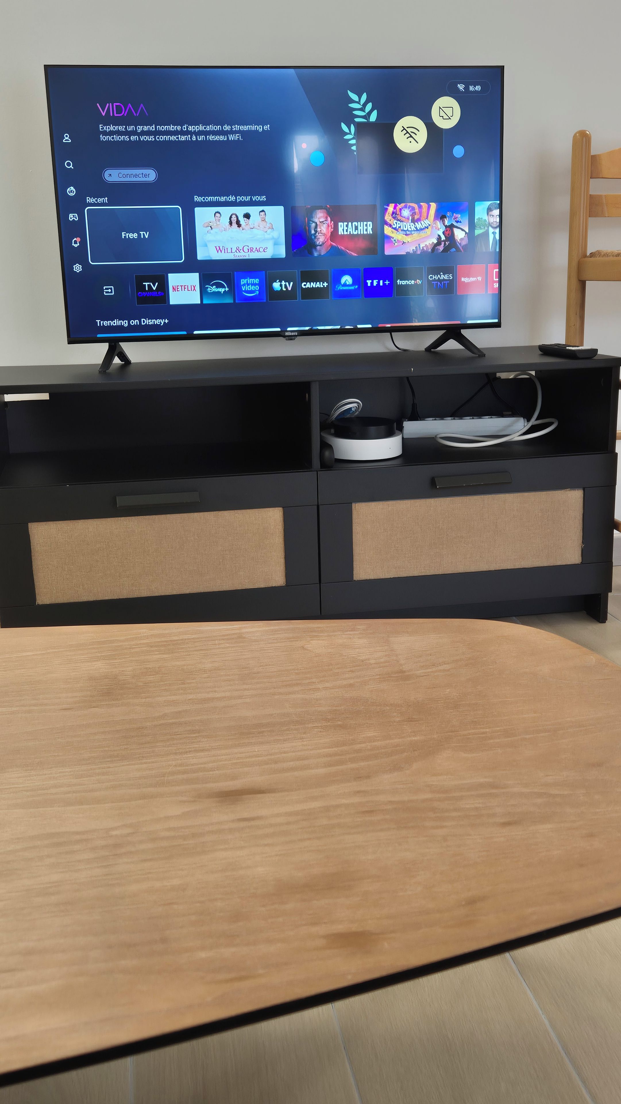 Musta, litteä näyttöinen televisio on sijoitettu mustalle viihdekeskukselle, ja sen edessä on puinen pöytä.